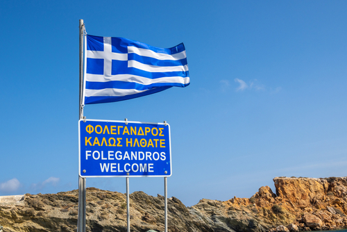 Greek,Flag,And,A,Board,Welcoming,Tourists,To,The,Island,Folegandros